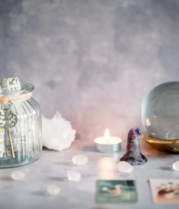 A serene setup with candles, tarot cards, crystals, and a flower jar on a soft surface.