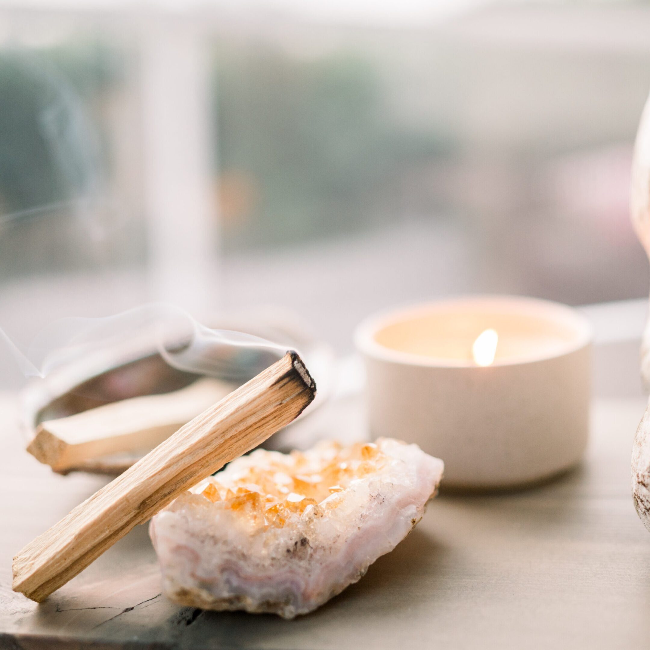 Candle, incense, and crystal on a serene surface near a window.